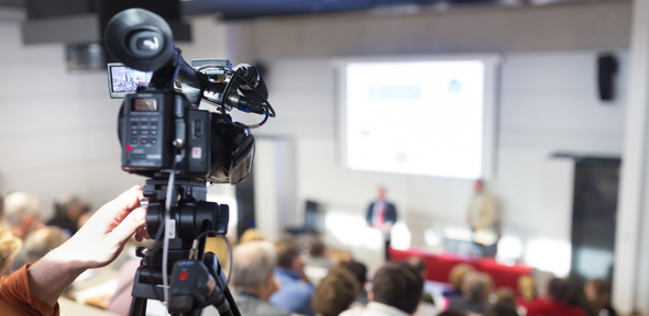 Video camera filming speaker in front of an audience