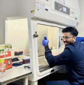 Researcher in navy lab coat sat at tissue culture hood in the lab