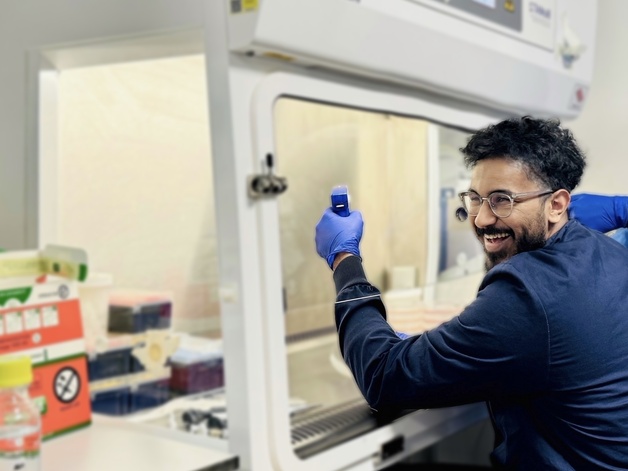 Researcher in navy lab coat sat at tissue culture hood in the lab